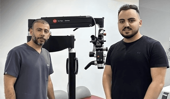 Two individuals with "Karl Kaps Microscopes made in Germany". One wears scrubs, the other a t-shirt.
