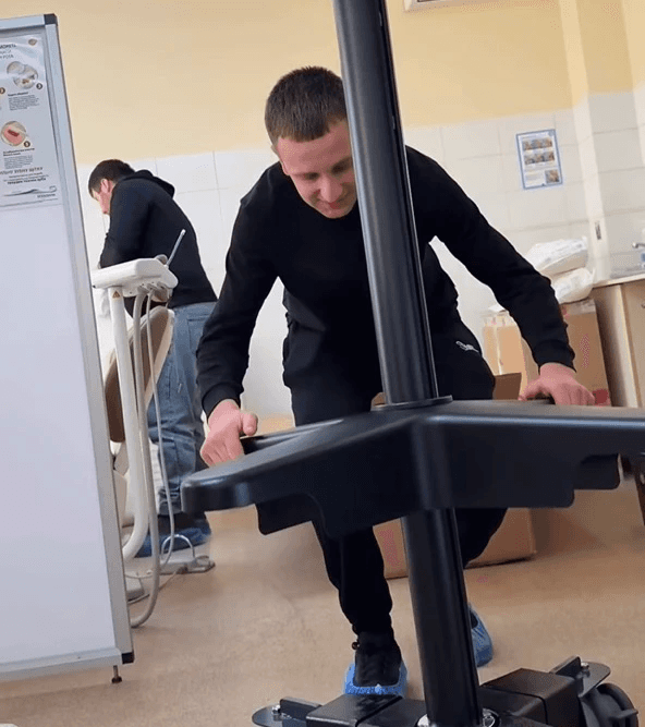 Eine Person schiebt einen Karl Kaps Mikroskope made in Germany Ständer mit blauen Überziehschuhen in einem